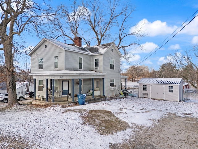 snow covered rear of property with covered porch and a shed