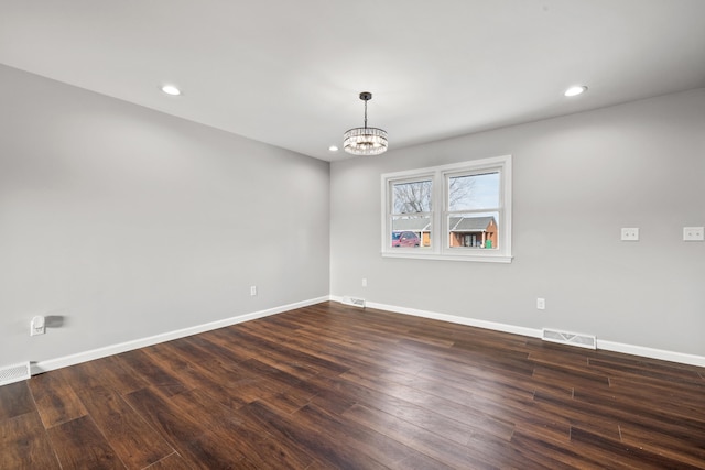 empty room featuring an inviting chandelier and dark hardwood / wood-style flooring