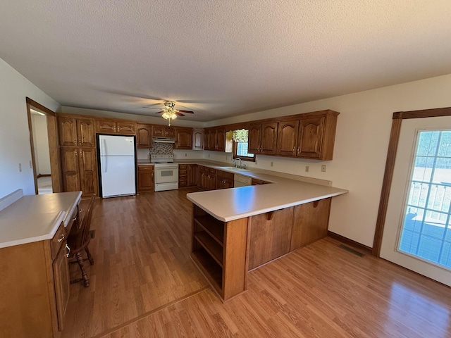 kitchen featuring sink, white appliances, light hardwood / wood-style floors, a textured ceiling, and kitchen peninsula