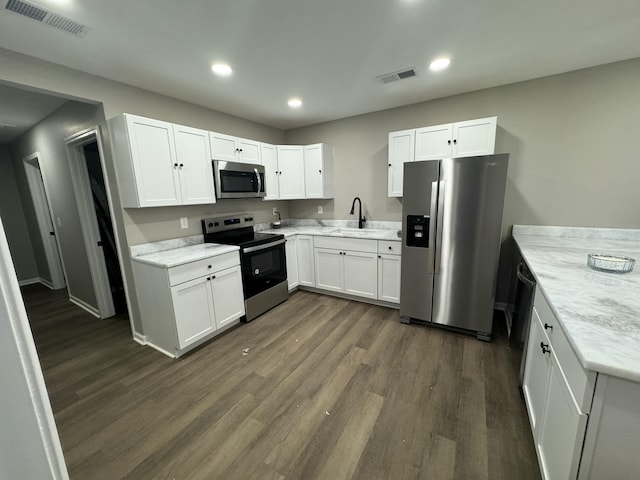 kitchen with sink, dark wood-type flooring, appliances with stainless steel finishes, light stone countertops, and white cabinets