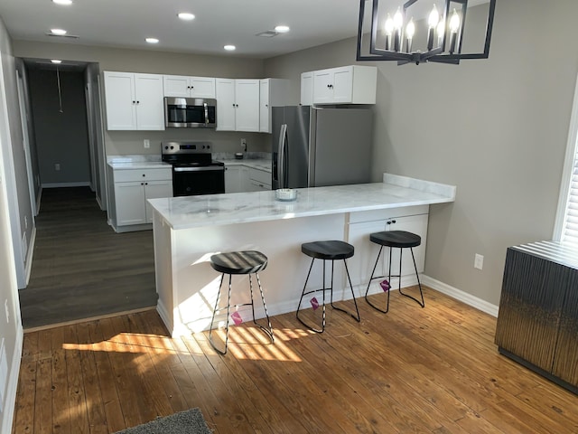 kitchen with pendant lighting, a breakfast bar area, appliances with stainless steel finishes, white cabinets, and kitchen peninsula