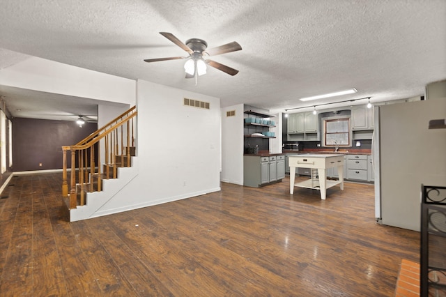 unfurnished living room featuring a textured ceiling, ceiling fan, dark hardwood / wood-style floors, and sink