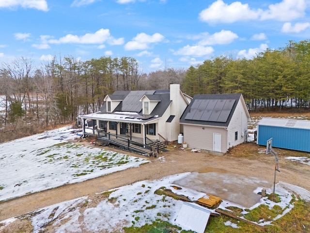 snow covered rear of property with a porch, a storage unit, and solar panels