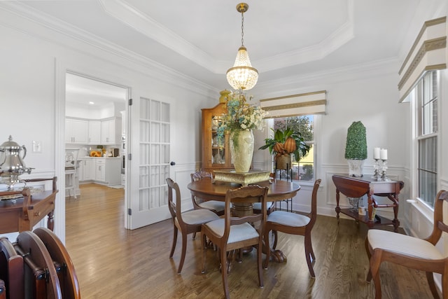 dining room featuring hardwood / wood-style flooring, ornamental molding, a raised ceiling, and a notable chandelier