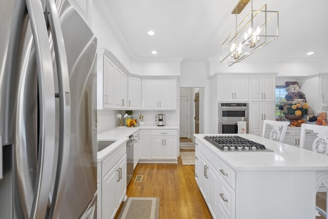 kitchen with white cabinetry, appliances with stainless steel finishes, decorative light fixtures, a kitchen breakfast bar, and a center island