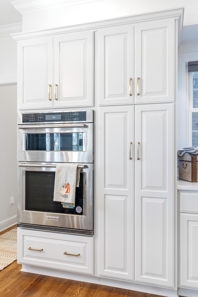 kitchen featuring stainless steel double oven, white cabinets, ornamental molding, and hardwood / wood-style floors