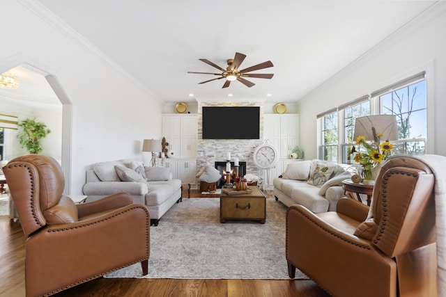 living room featuring ceiling fan, wood-type flooring, a fireplace, and ornamental molding