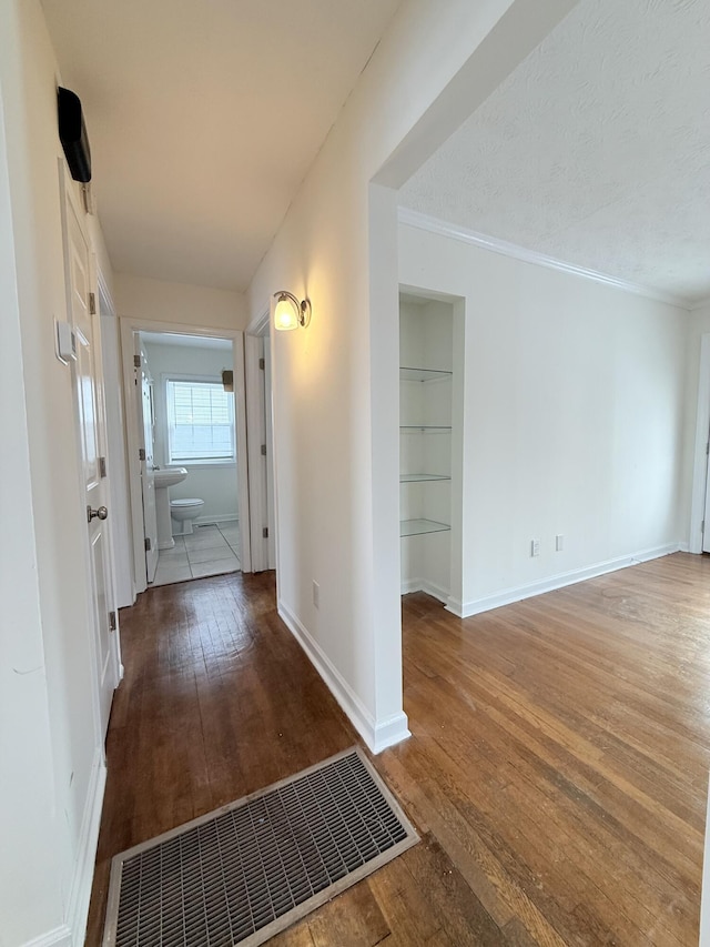 corridor with crown molding, wood-type flooring, built in features, and a textured ceiling