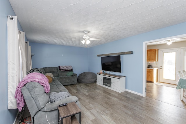 living room with ceiling fan, a textured ceiling, and light wood-type flooring