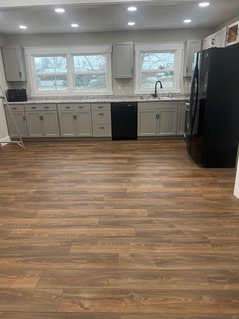 kitchen with dark wood-style floors, recessed lighting, a sink, light stone countertops, and black appliances