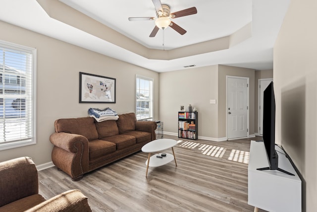 living room with ceiling fan, a raised ceiling, and light hardwood / wood-style floors