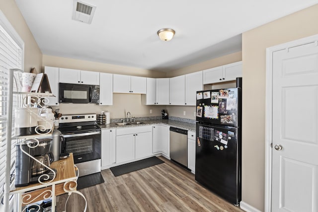 kitchen with black appliances, wood-type flooring, white cabinets, sink, and dark stone counters