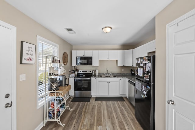 kitchen with sink, black appliances, white cabinets, and wood-type flooring