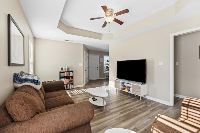 living room featuring ceiling fan, wood-type flooring, and a tray ceiling