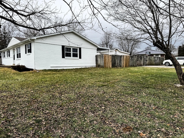 view of side of home featuring a yard, brick siding, and fence