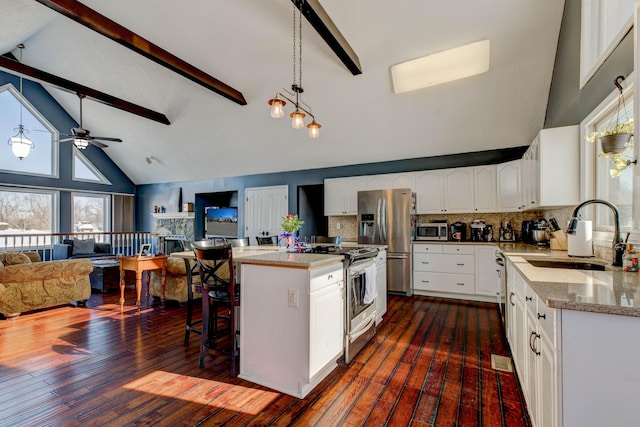 kitchen with appliances with stainless steel finishes, a kitchen island, white cabinetry, beamed ceiling, and backsplash