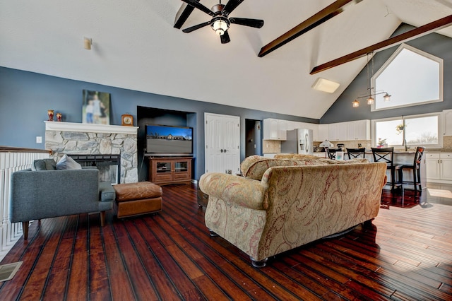 living room featuring wood-type flooring, ceiling fan, a stone fireplace, high vaulted ceiling, and beamed ceiling