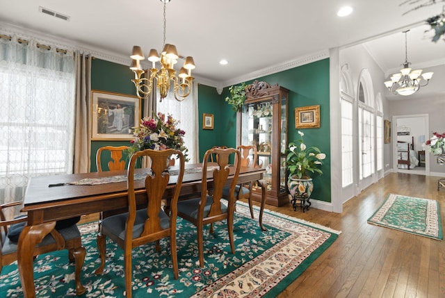 dining area featuring wood-type flooring, a healthy amount of sunlight, a notable chandelier, and ornamental molding