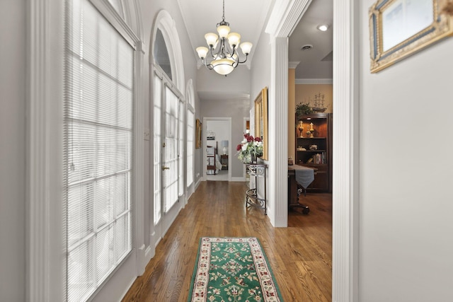 corridor with crown molding, wood-type flooring, and a notable chandelier