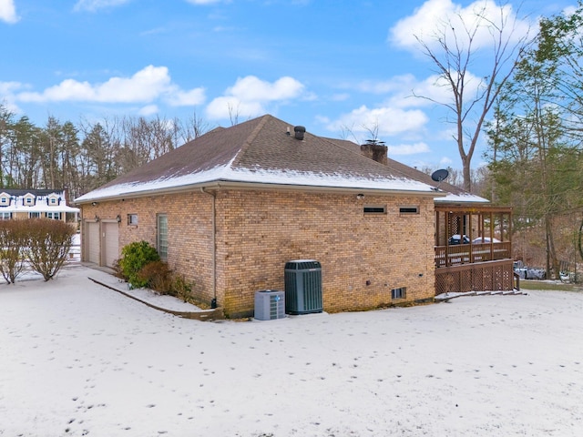 snow covered property featuring a garage and central AC unit