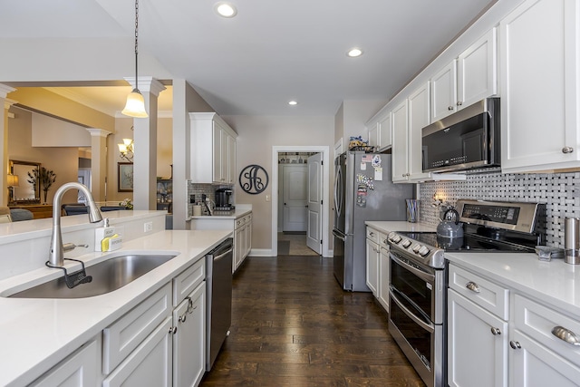 kitchen with appliances with stainless steel finishes, a sink, decorative columns, and white cabinets