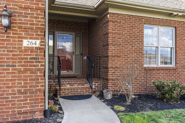 entrance to property with a shingled roof and brick siding