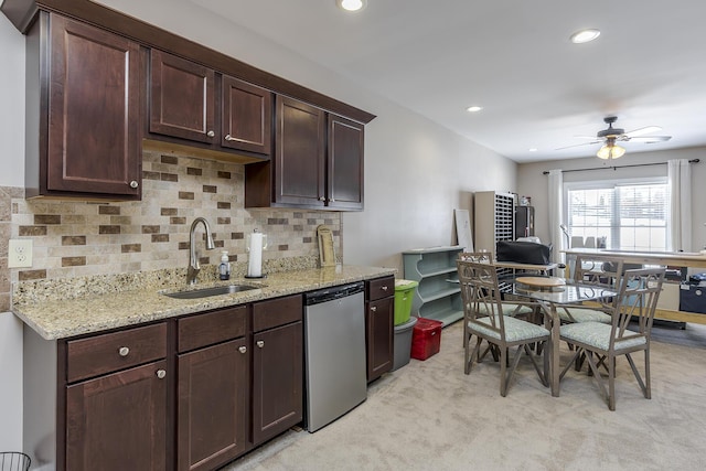 kitchen with tasteful backsplash, stainless steel dishwasher, dark brown cabinetry, a sink, and light stone countertops