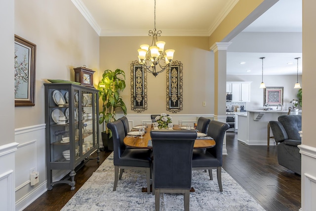 dining room with wainscoting, dark wood-style flooring, an inviting chandelier, crown molding, and ornate columns