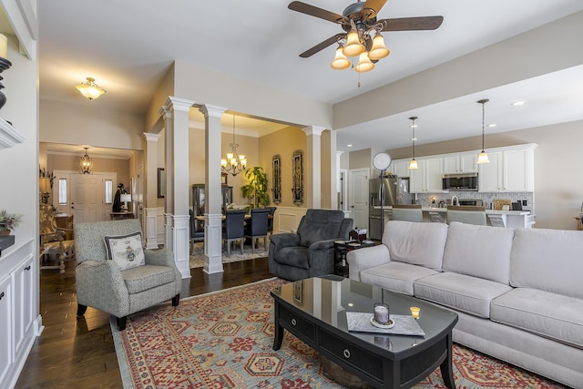 living room featuring dark wood-style floors, a wainscoted wall, ceiling fan with notable chandelier, and decorative columns