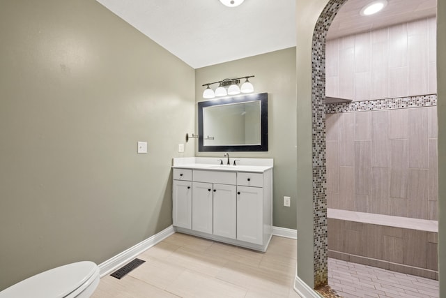 bathroom featuring vanity, toilet, tiled shower, and tile patterned flooring