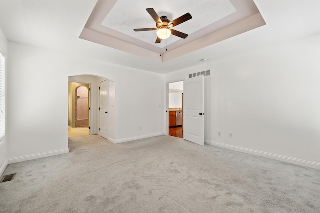 unfurnished room with light carpet, ceiling fan, and a raised ceiling