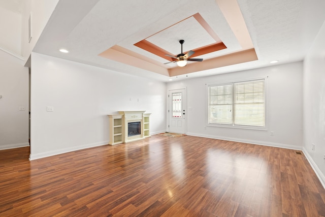 unfurnished living room featuring ceiling fan, a textured ceiling, dark hardwood / wood-style floors, and a tray ceiling