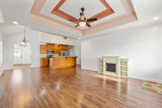 unfurnished living room with ceiling fan, a raised ceiling, and dark wood-type flooring