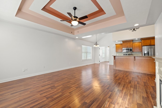 unfurnished living room with ceiling fan with notable chandelier, dark hardwood / wood-style flooring, and a tray ceiling