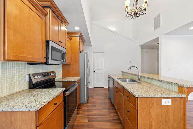 kitchen with light stone countertops, appliances with stainless steel finishes, sink, pendant lighting, and dark hardwood / wood-style flooring