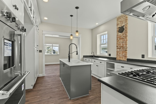 kitchen with refrigerator, range hood, decorative light fixtures, white cabinetry, and a kitchen island with sink