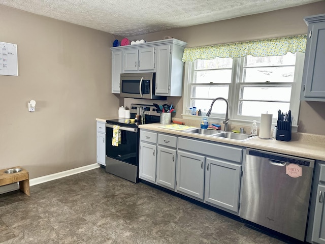 kitchen with stainless steel appliances, sink, gray cabinetry, and a textured ceiling