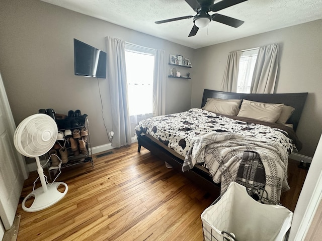 bedroom with multiple windows, wood-type flooring, ceiling fan, and a textured ceiling