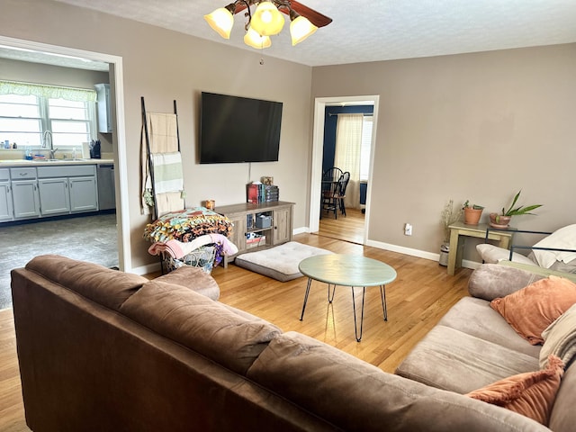 living room with ceiling fan, sink, a textured ceiling, and light hardwood / wood-style floors