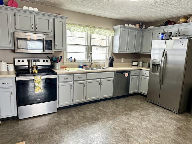 kitchen with stainless steel appliances, sink, a textured ceiling, and gray cabinetry