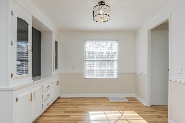 unfurnished dining area with light wood-type flooring and a notable chandelier