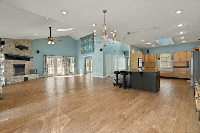 kitchen with a spacious island, a skylight, light hardwood / wood-style floors, a kitchen breakfast bar, and high vaulted ceiling