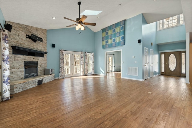 unfurnished living room featuring hardwood / wood-style floors, a skylight, a fireplace, ceiling fan, and high vaulted ceiling