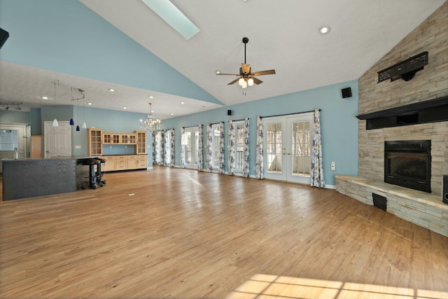 unfurnished living room with french doors, light wood-type flooring, a fireplace, ceiling fan with notable chandelier, and high vaulted ceiling