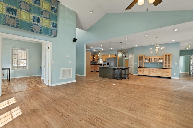 unfurnished living room featuring light hardwood / wood-style floors, a towering ceiling, and ceiling fan with notable chandelier