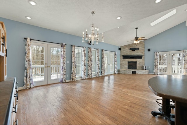 unfurnished living room with vaulted ceiling with skylight, a stone fireplace, french doors, and light wood-type flooring