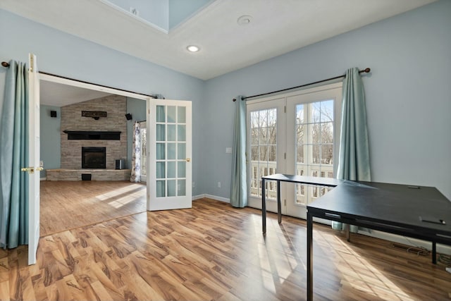 office space featuring a stone fireplace, light wood-type flooring, lofted ceiling, and french doors