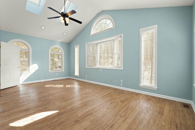 empty room with ceiling fan, lofted ceiling with skylight, and light hardwood / wood-style floors