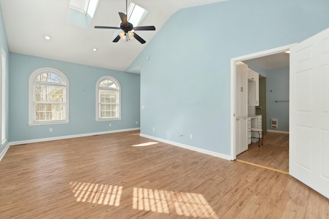 spare room featuring light wood-type flooring, a skylight, high vaulted ceiling, and ceiling fan