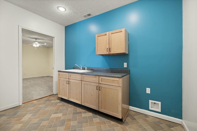 kitchen with light brown cabinetry, ceiling fan, sink, carpet flooring, and a textured ceiling